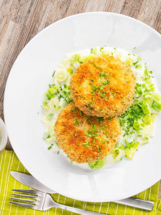 Overhead golden salmon and sardine fish cakes served with creamed leeks.