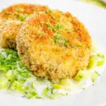 Crispy golden salmon and sardine fish cakes served with creamed leeks featuring a title overlay.