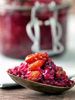 Close-up red cabbage chutney with large golden raisins on a spoon.