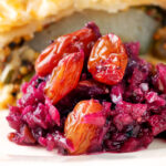 Close-up red cabbage chutney with large golden raisins served with a pie.