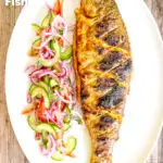 Overhead whole tandoori trout fish that has been cooked on a BBQ featuring a title overlay.