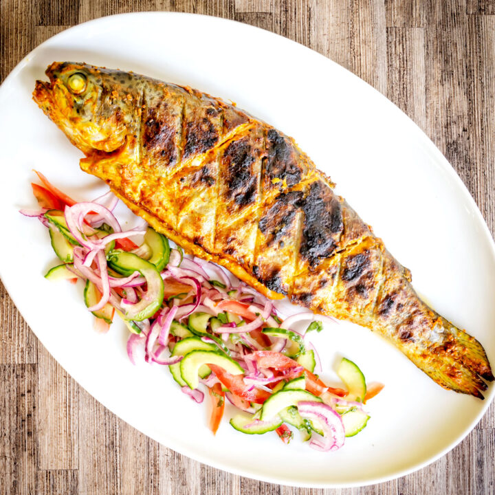 Whole tandoori fish (trout) that has been cooked on a BBQ served with a salad.