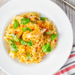 Overhead tomato and salmon fillet pasta with basil and crispy bread crumbs.