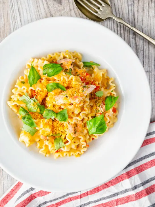 Overhead tomato and salmon fillet pasta with basil and crispy bread crumbs.