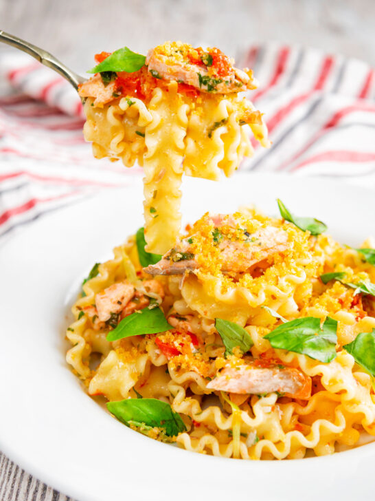 Tomato and salmon fillet pasta with basil and crispy bread crumbs on a fork.