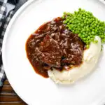 Overhead braised steak and onions served with mashed potato and peas.