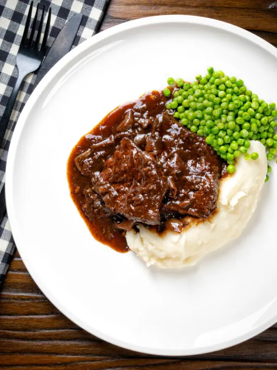 Overhead braised steak and onions served with mashed potato and peas.