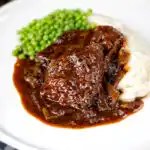 Braised steak and onions served with mashed potato and peas.