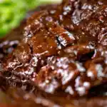 Close-up braised steak and onions served with mashed potato and peas.