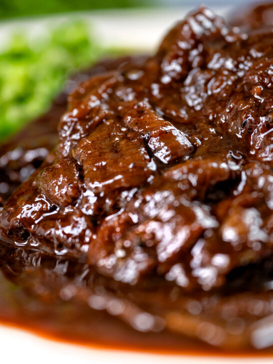 Close-up braised steak and onions served with mashed potato and peas.