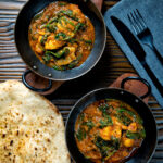 Overhead Indian inspired chicken saag or saagwala curry served with naan bread.