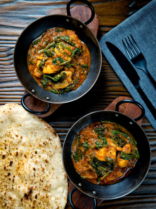 Overhead Indian inspired chicken saag or saagwala curry served with naan bread.