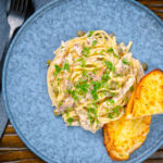 Overhead creamy lemon chicken pasta served with cheesy garlic bread.