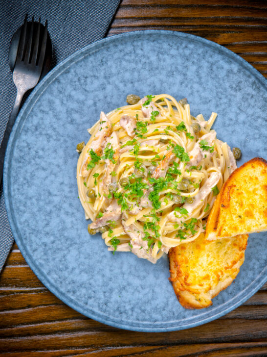 Overhead creamy lemon chicken pasta served with cheesy garlic bread.