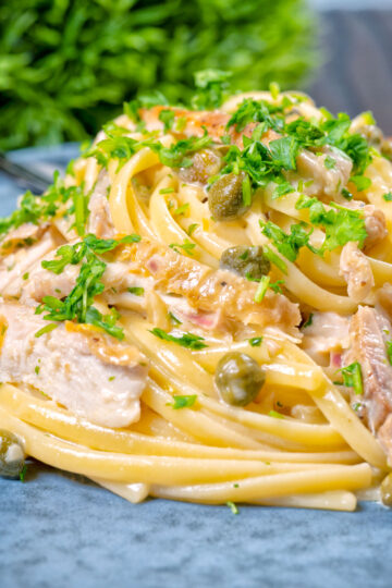 Close-up creamy lemon chicken pasta with capers and parsley.