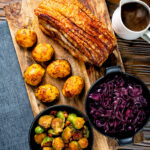 Overhead slow roast pork belly with crackling, roast potatoes, sprouts, red cabbage and gravy.