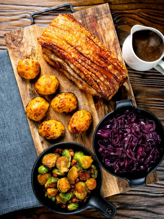 Overhead slow roast pork belly with crackling, roast potatoes, sprouts, red cabbage and gravy.