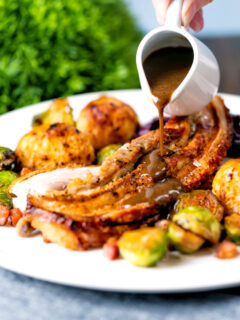 Cider gravy being poured over a slow roasted crispy pork belly Sunday lunch.