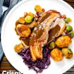 Overhead slowly roasted pork belly, roast potatoes, sprouts, red cabbage and cider gravy featuring a title overlay.