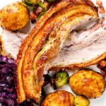 Overhead close-up slow roast pork belly, roast potatoes, miso sprouts and red cabbage.
