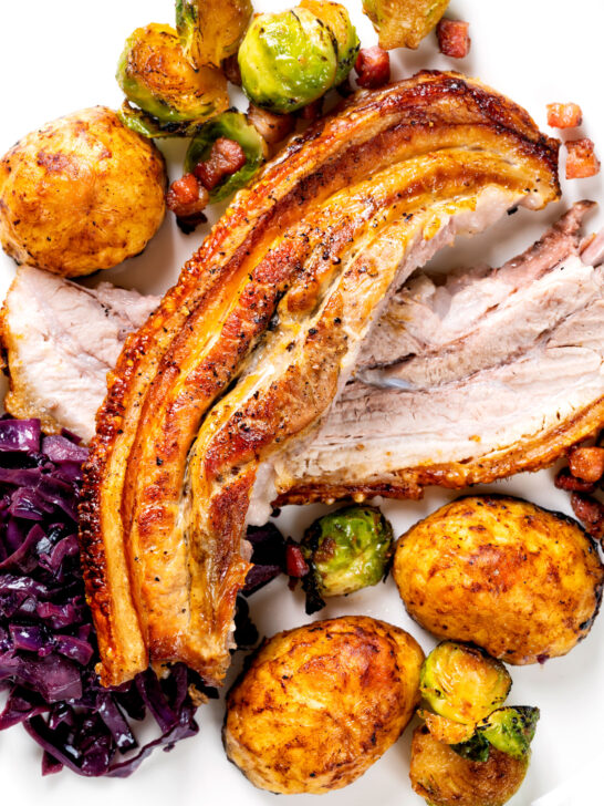 Overhead close-up slow roast pork belly, roast potatoes, miso sprouts and red cabbage.