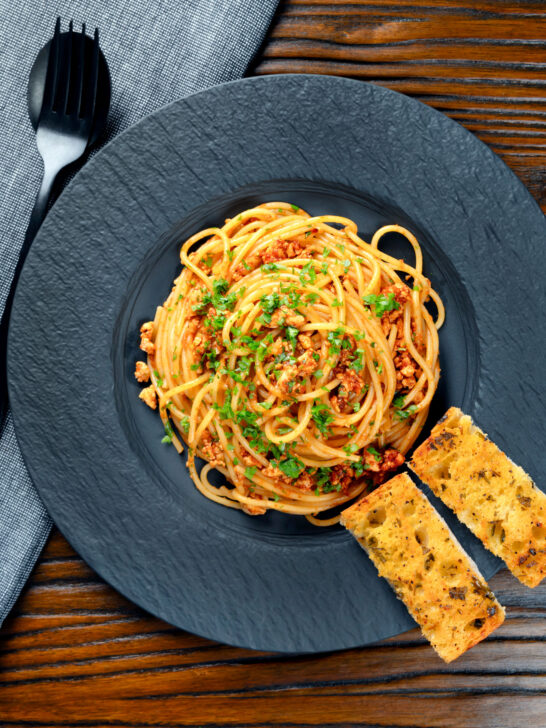 Overhead crumbled tofu pasta in a spiced tomato sauce served with garlic bread.