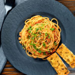 Overhead crumbled tofu pasta in a spiced tomato sauce served with garlic bread featuring a title overlay.