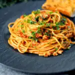 Crumbled tofu pasta in a spiced tomato sauce served with garlic bread featuring a title overlay.