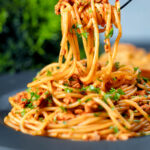 Crumbled tofu pasta in a spiced tomato sauce being picked up with a fork.