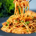 Crumbled tofu pasta in a spiced tomato sauce being picked up with a fork.