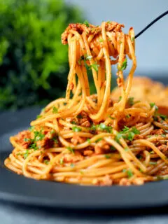 Crumbled tofu pasta in a spiced tomato sauce being picked up with a fork.