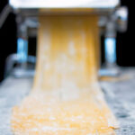 Homemade duck egg pasta being cut into tagliatelle in a pasta machine.