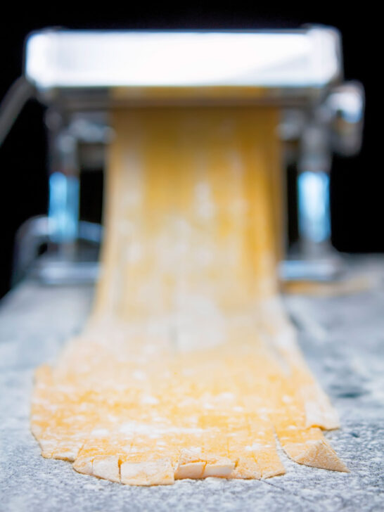 Homemade duck egg pasta being cut into tagliatelle in a pasta machine.