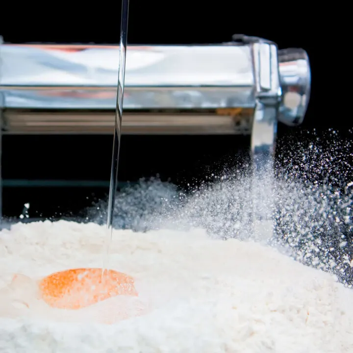 A duck egg being dropped into flour to with a pasta machine in the background.