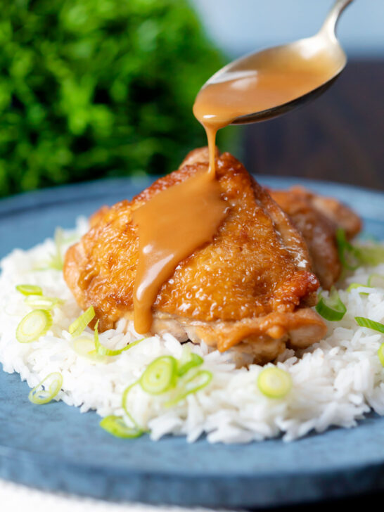 Coconut milk adobo sauce being poured over braised chicken thighs.