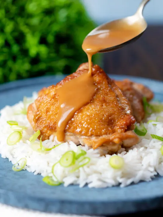 Coconut milk adobo sauce being poured over braised chicken thighs.