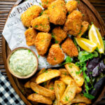 Overhead fish goujons or nuggets made with monkfish served with tartar sauce and wedges featuring a title overlay.