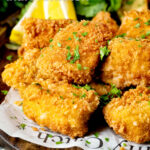 Close up fish goujons or nuggets made with monkfish served with lemon wedges featuring a title overlay.