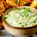 Close-up homemade tartar sauce served with fish goujons and potato wedges.