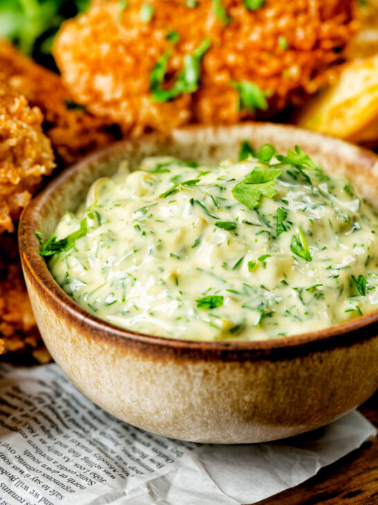 Close-up homemade tartar sauce served with fish goujons and potato wedges.