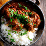 Overhead lamb rogan josh curry with rice, naan and fresh coriander.