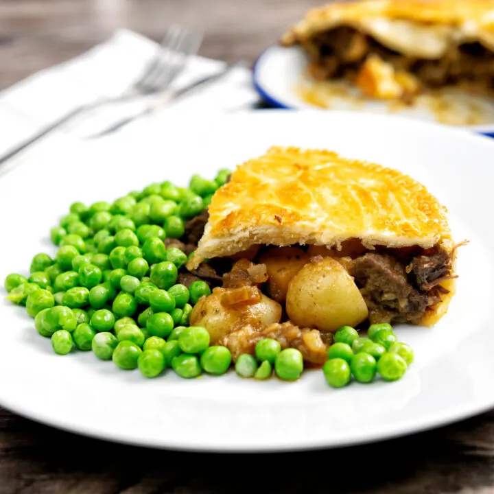 A slice of traditional meat and potato plate pie served with peas.