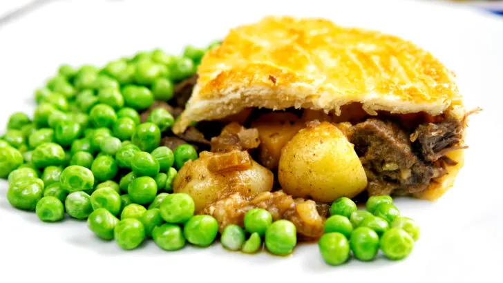 A slice of traditional meat and potato plate pie served with peas.