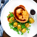 Overhead homemade minced beef and onion pie served with peas and potatoes.