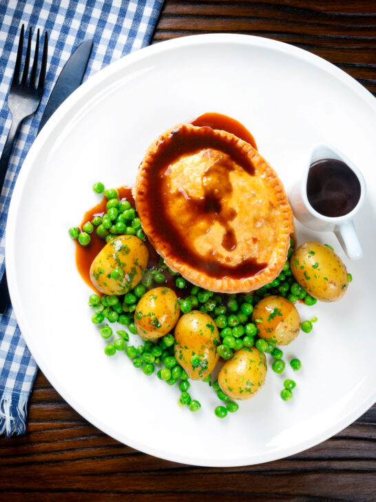 Overhead homemade minced beef and onion pie served with peas and potatoes.