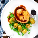 Overhead homemade minced beef and onion pie served with peas and potatoes featuring a title overlay.