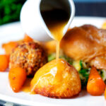 Roasted chicken gravy being poured over perfect Sunday lunch roast potatoes.