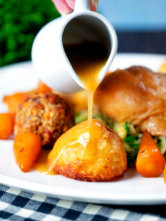 Roasted chicken gravy being poured over perfect Sunday lunch roast potatoes.