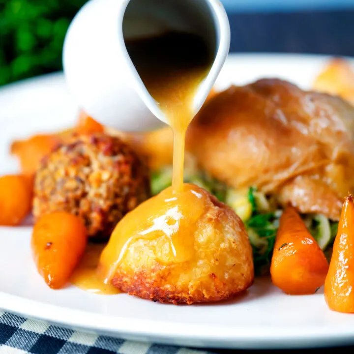 Roasted chicken pan gravy being poured over perfect Sunday lunch roast potatoes.