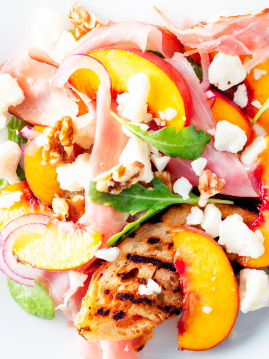 Close-up overhead main course summer salad with pickled peaches, ham and goats cheese.